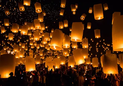 Hundreds of glowing paper lanterns rising above a crowd at Chiang Mai's Yi Peng festival.